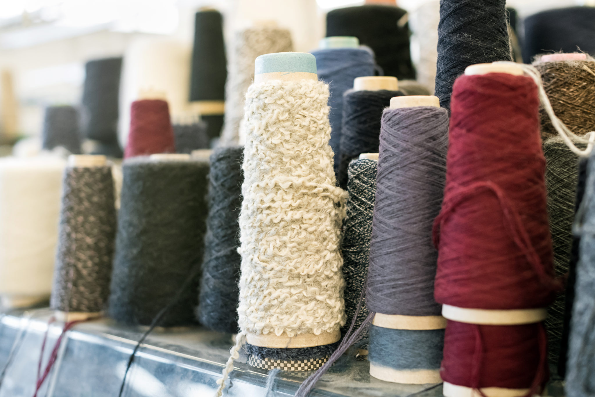 Spools and reels of spun cashmere wool or yarn in assorted colors and textures on a shelf in close up