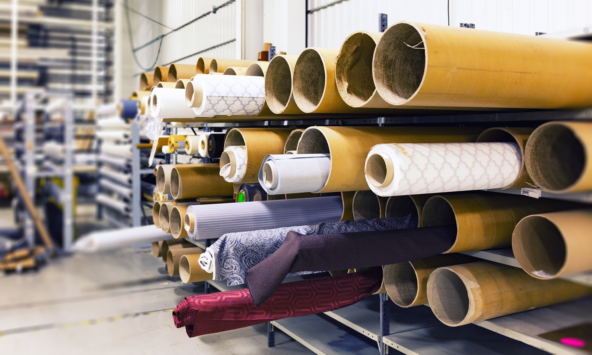 A well-organized textile warehouse with numerous rolls of fabric in various colors and patterns stored on shelves.