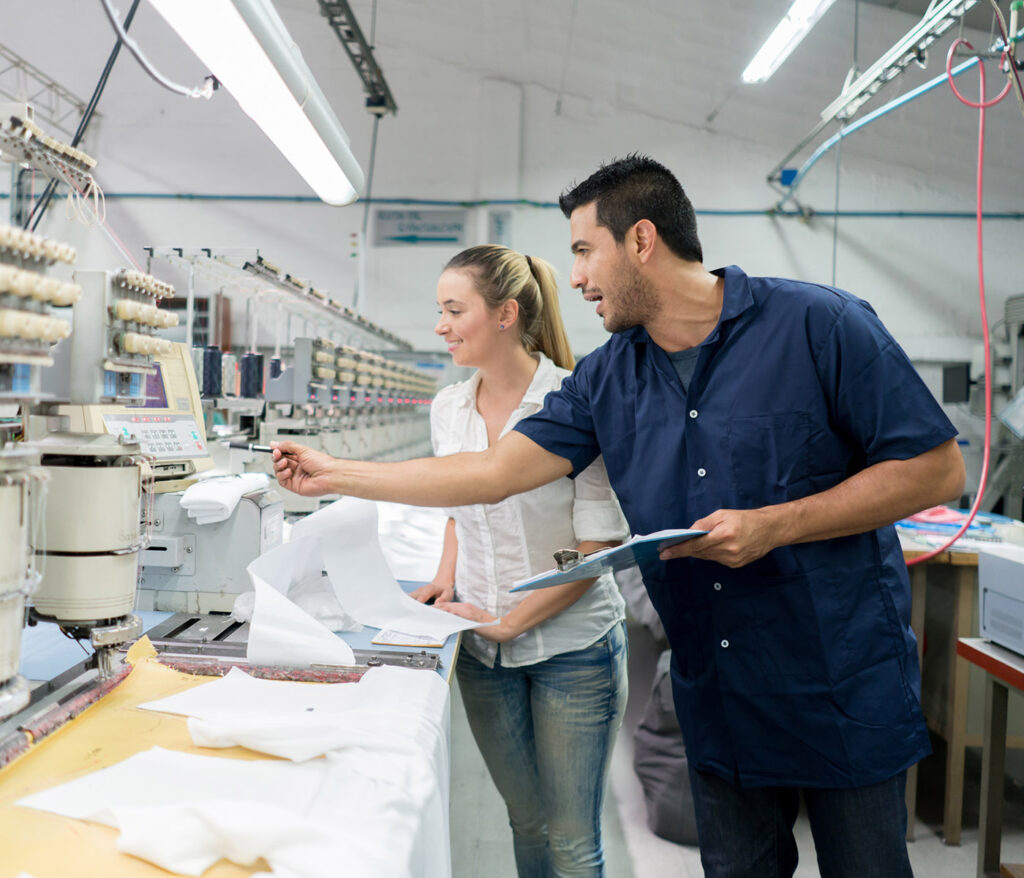 Business owner and manual worker working at an embroidery factory supervising the machines as they work.